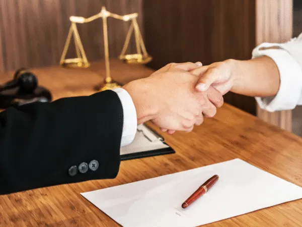 "Lawyer and client shaking hands across a legal desk with documents and justice scales in the background." best-wrongful-termination-attorney-in-los-angeles/