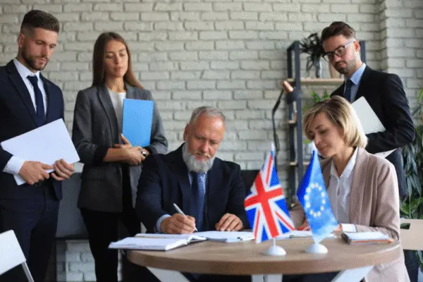 "Group of business professionals witnessing a formal agreement signing between representatives of the UK and European Union, with flags on the table.Experienced wrongful termination attorney representing San Diego clients