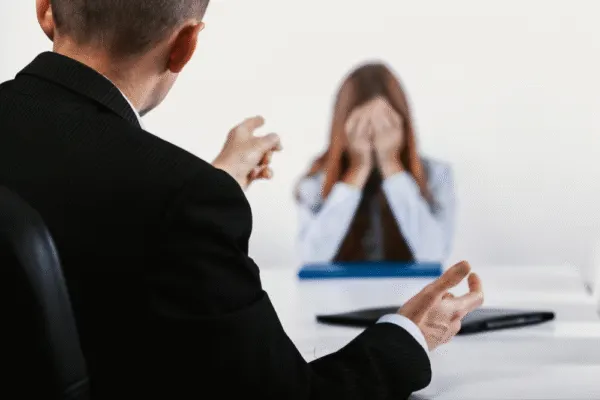 Man in a suit reprimanding a distressed woman covering her face in a workplace settingSan Diego wrongful termination lawyer consulting client